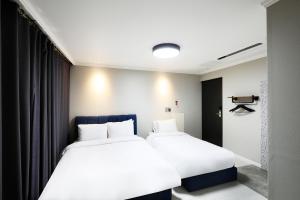 two beds in a hotel room with white sheets at Cornerstone Hotel in Seogwipo