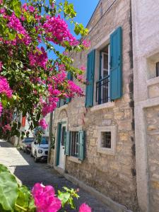ein Steingebäude mit blauen Fensterläden und rosa Blumen in der Unterkunft Özel tasarımlı TARİHİ TAŞ EV in Cesme