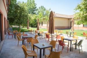 un patio con mesas, sillas y sombrillas en Hotel Real Balneario Carlos III en Trillo