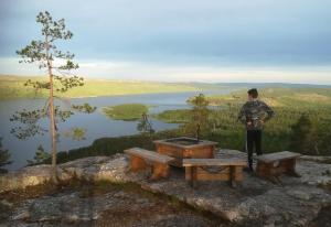 a man standing on a rock with a picnic table and a lake at House next door the Arctic Circle in Överkalix