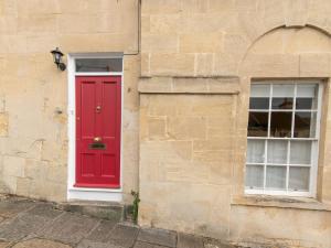a red door and two windows on a stone building at Pass the Keys Cosy 1 Bed Studio in Central Bath in Bath