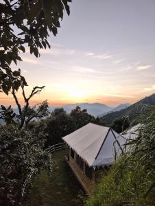 ein Zelt auf einem Feld mit Sonnenuntergang im Hintergrund in der Unterkunft DugDug Camps - Glamping Amidst Nature in Bhīm Tāl