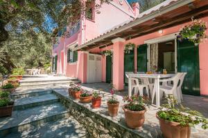 una casa rosa con una mesa y macetas en Elies Villa Corfu, en Áno Garoúna