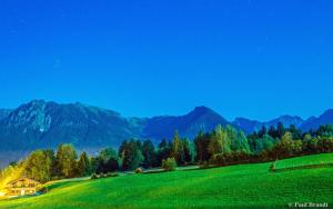 a house on a green hill with mountains in the background at Baldauf's Alpchalet in Oberstdorf