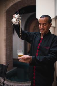 a man holding a glass of beer and holding a drink at Riad Les Trois Palmiers El Bacha in Marrakech