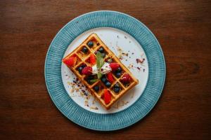 a plate of waffles with berries and whipped cream at OREA Hotel Angelo Praha in Prague