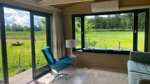 ein Wohnzimmer mit einem blauen Stuhl und großen Fenstern in der Unterkunft Chalet "naast de Schoppe" in Aalten