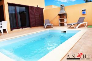 a swimming pool in front of a house with a fireplace at Anahi Home Corralejo - Villa Cardon 12 in La Oliva