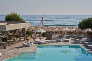 una piscina con sedie, ombrelloni e oceano di Atlantica Amalthia Beach Hotel - Adults Only ad Agia Marina Nea Kydonias