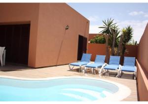 a swimming pool with blue chairs and a building at Anahi Homes Corralejo - Villa Drago 12 in La Oliva