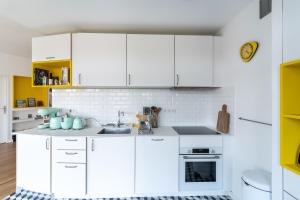 a white kitchen with white cabinets and yellow accents at THE BUILDING - Appartement d'architecte avec vue Notre Dame de la Garde in Marseille