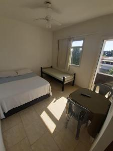 a bedroom with a bed and a table and a window at Pousada Campo Verde in Guarapari