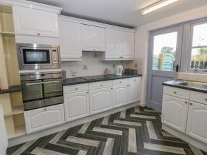 a kitchen with white cabinets and stainless steel appliances at Dwyros in Pwllheli