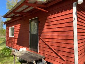 a red house with a wooden door and a wooden bench at Trevlig Röd liten stuga in Ryd