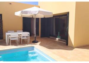 een terras met een tafel en een parasol naast een zwembad bij Anahi Homes Corralejo- Bicacarera 9 in La Oliva
