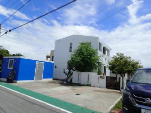 a white and blue house with a car parked next to it at Smilax Kurichi in Uruma