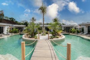 a resort pool with a wooden walkway and palm trees at Kalia Bingin - Adult only in Uluwatu