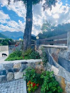 un albero e un muro di pietra con fiori e un gatto di Guesthouse AlpenRose a Mestia