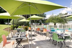 eine Terrasse mit Tischen, Stühlen und grünen Sonnenschirmen in der Unterkunft Holiday Inn Lille Ouest Englos, an IHG Hotel in Englos