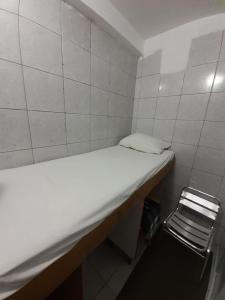 Habitación pequeña con cama blanca y silla en Hostel Residencial, en São Paulo