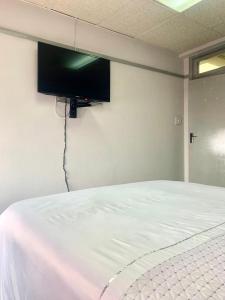 a bedroom with a white bed with a flat screen tv on the wall at Stay Inn Lodge Randfontein in Randfontein