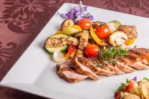 a white plate of food with meat and vegetables at Hotel Lázně Kostelec in Zlín