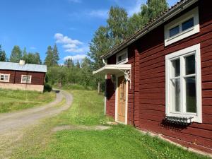 a red house with a white door and a dirt road at Bogärdan, cozy cabin by the Luleå River in Harads