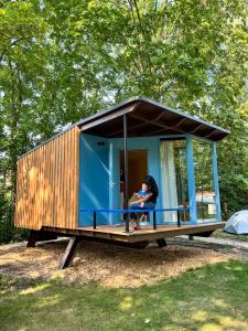 une femme assise sur la terrasse couverte d'une petite maison dans l'établissement Camping Vliegenbos, à Amsterdam