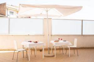 twee witte tafels en stoelen onder een paraplu bij G&G Hotel in Grammichele
