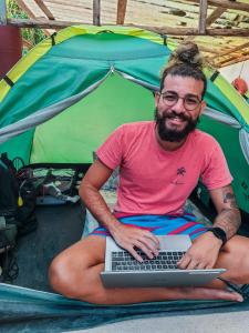 a man sitting in front of a tent with a laptop at Ready Camp e Suítes da Cachoeira in Abraão