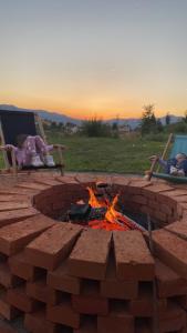 eine Feuerstelle mit zwei Leuten, die um sie herum auf Gartenstühlen sitzen in der Unterkunft Cortina resort in Ivanjica
