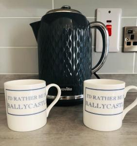 two coffee mugs sitting on a counter with a kettle at Ballycastle Town Centre Studio Apartment in Ballycastle