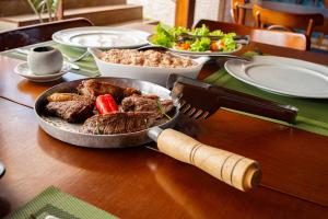 una mesa con una sartén de carne y una ensalada en Pousada Mahalo Fulô, en Galos