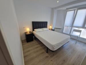 a bedroom with a white bed and two windows at 150A Apartamento moderno, Playa San Lorenzo in Gijón