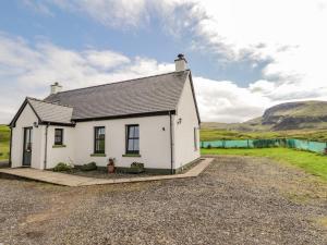 a white house with a hill in the background at Ridge End Cottage in Kilmaluag