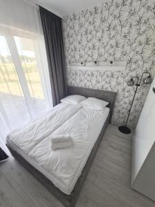 a bedroom with a bed with white sheets and wallpaper at Apartamenty Morze u Sary in Dziwnówek