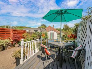 a patio table with a green umbrella on a deck at Holly Cottage in Swaffham