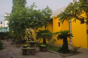 ein gelbes Gebäude mit Bäumen und Bänken im Innenhof in der Unterkunft Airport X Managua in Managua