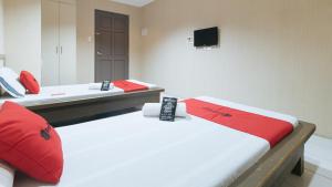 a room with two beds with red pillows and a television at RedDoorz @ Bridgeway Hotel Tuguegarao City in Tuguegarao City