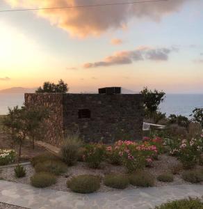 a stone building with flowers in front of the ocean at Loutra Olive Garden Stone House #3 in Mandrakion