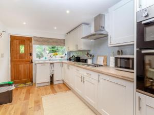 a white kitchen with white cabinets and a wooden floor at Fox Bank Cottage in Macclesfield