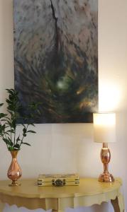 a table with a lamp and a painting on the wall at Porcupine Hills Olive and Guest Farm in Botrivier