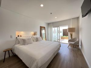a white bedroom with a large bed and a chair at Alojamento White Rose Boutique in Zambujeira do Mar