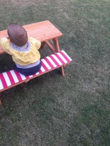 una niñita sentada en un banco junto a una mesa de picnic en Guest House Edelweiss, en Koprivshtitsa