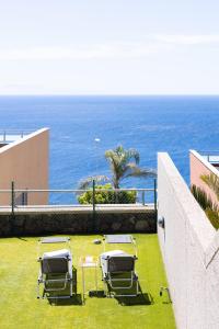 Chalet con vistas al mar en Santa Cruz de Tenerife في سانتا كروث دي تينيريفه: مجموعة من الكراسي جالسة على العشب بالقرب من المحيط