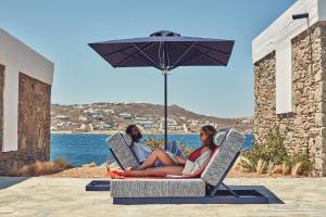 two people sitting in chairs under an umbrella at Mykonos Theoxenia, a member of Design Hotels in Mikonos