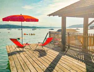 two chairs and an umbrella on a dock with the water at Villa Gabriela in Pörtschach am Wörthersee