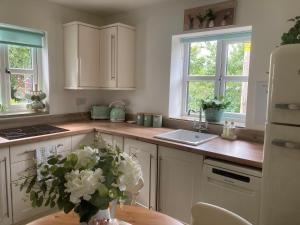a kitchen with white cabinets and a table with a vase of flowers at Cosy country cottage with outdoor bathing in Halkyn