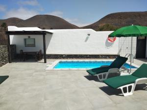 a swimming pool with two chairs and an umbrella at Finca La Tabaiba Apartamento alto in Máguez