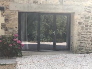uma grande porta de vidro num edifício de pedra com flores em Le gîte de l'Ajon em Landes-sur-Ajon